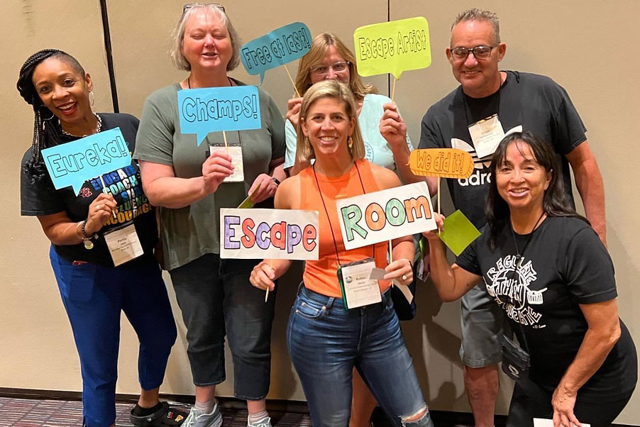 Teachers holding up signs saying "Escape Room" and posing at the National Energy Educators Conference